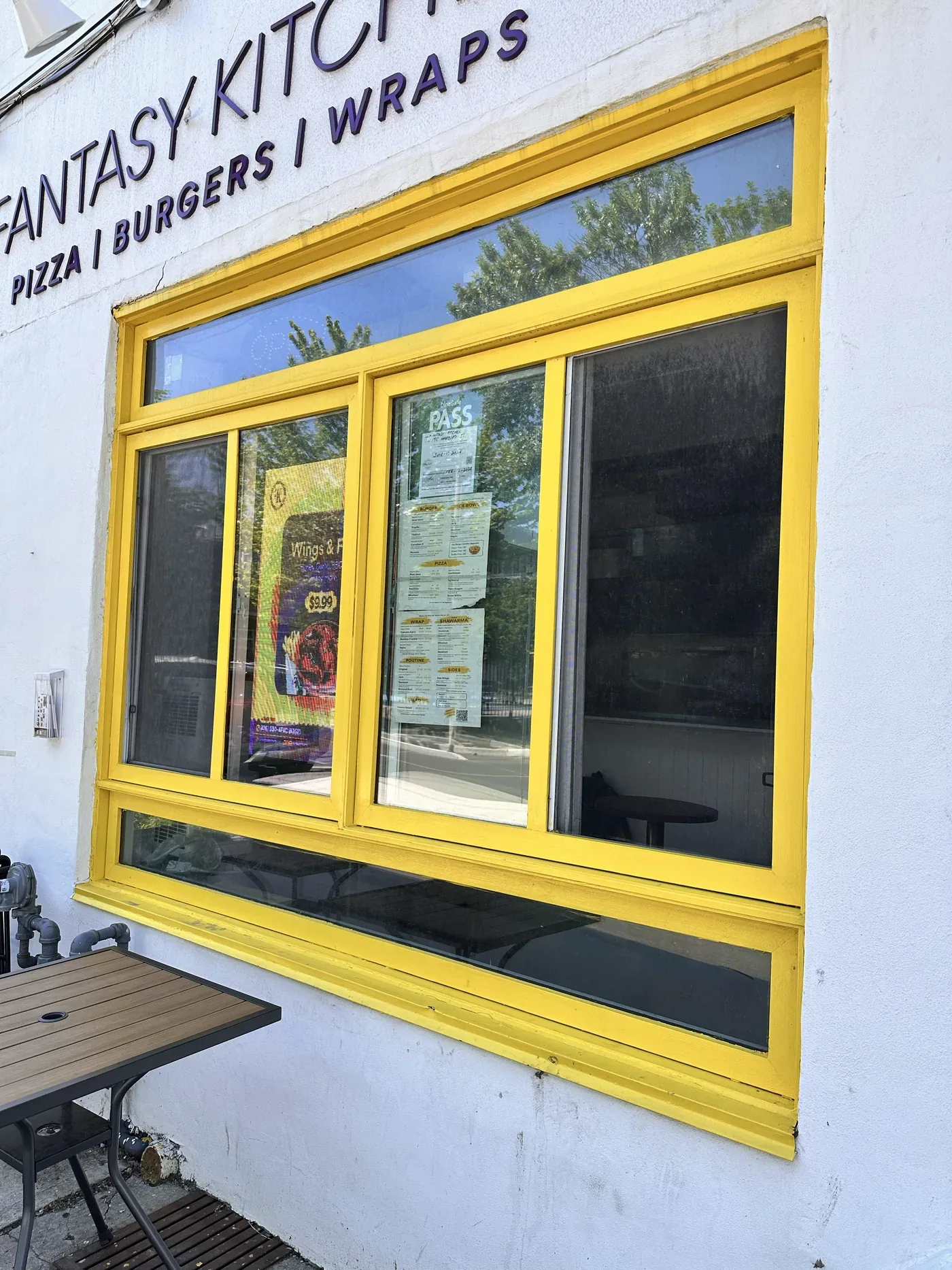 The yellow shopfront window on Harbord Street, with the $9.99 combo poster inside and a table on the pavement